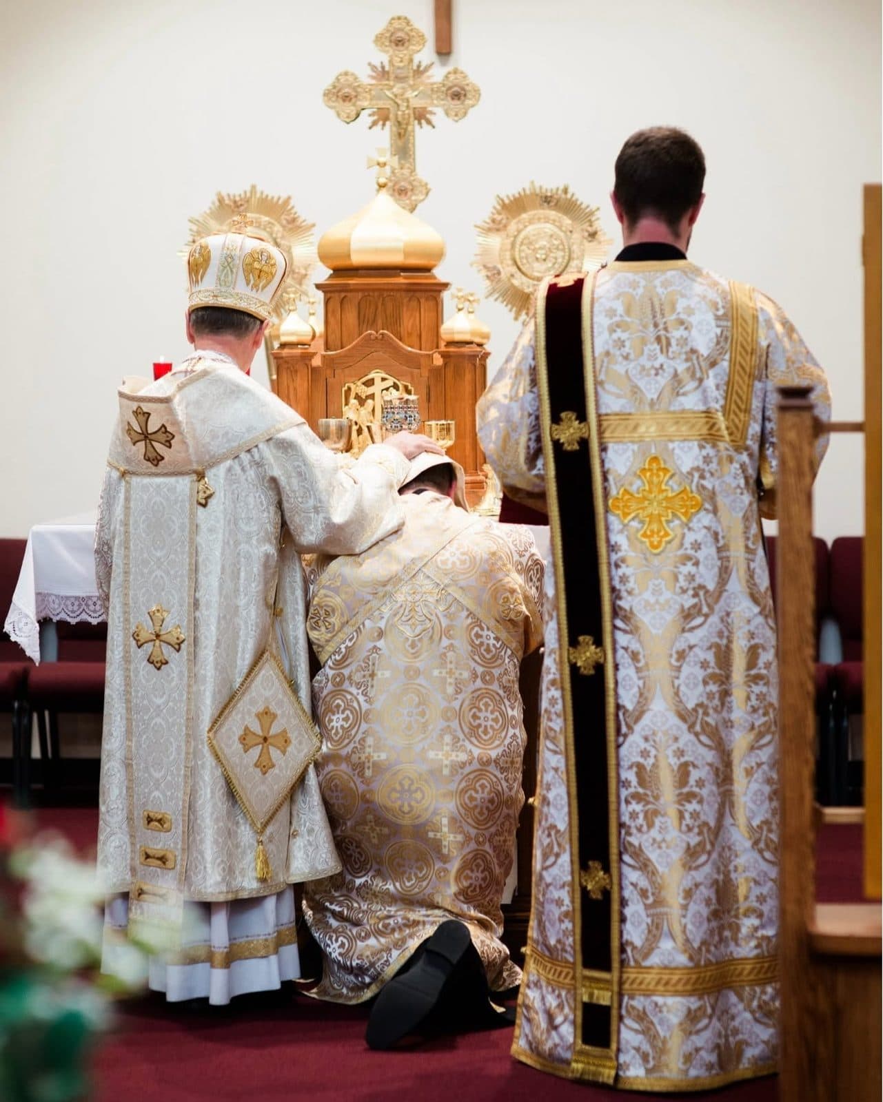Vested clergy gather around a kneeling minister during a solemn liturgical service.