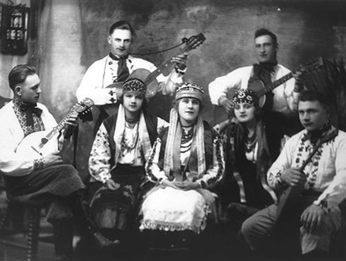 Seven musicians in traditional Ukrainian clothing play instruments in a studio portrait.