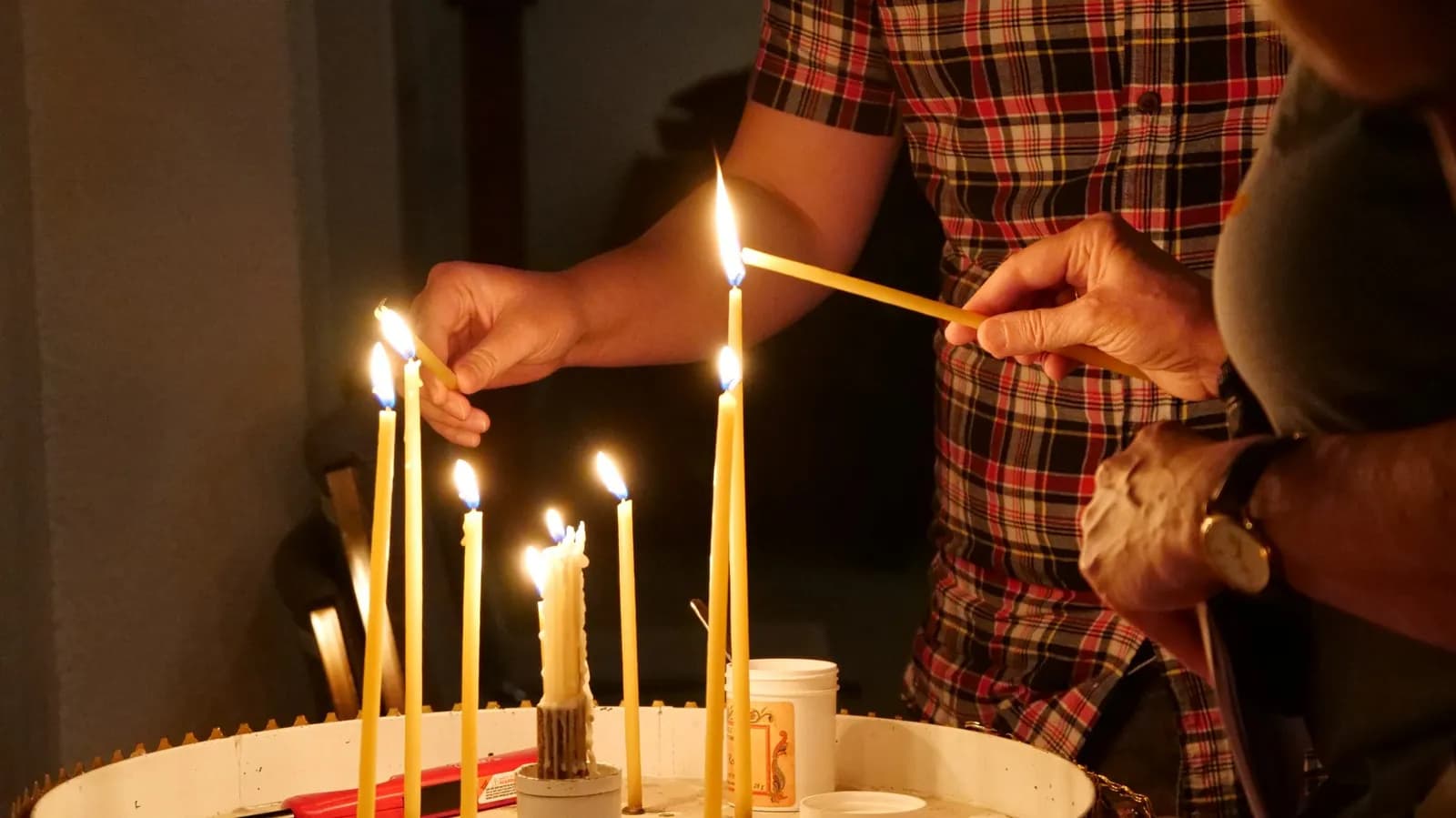 Hands light tall beeswax candles in a church, with flames flickering.