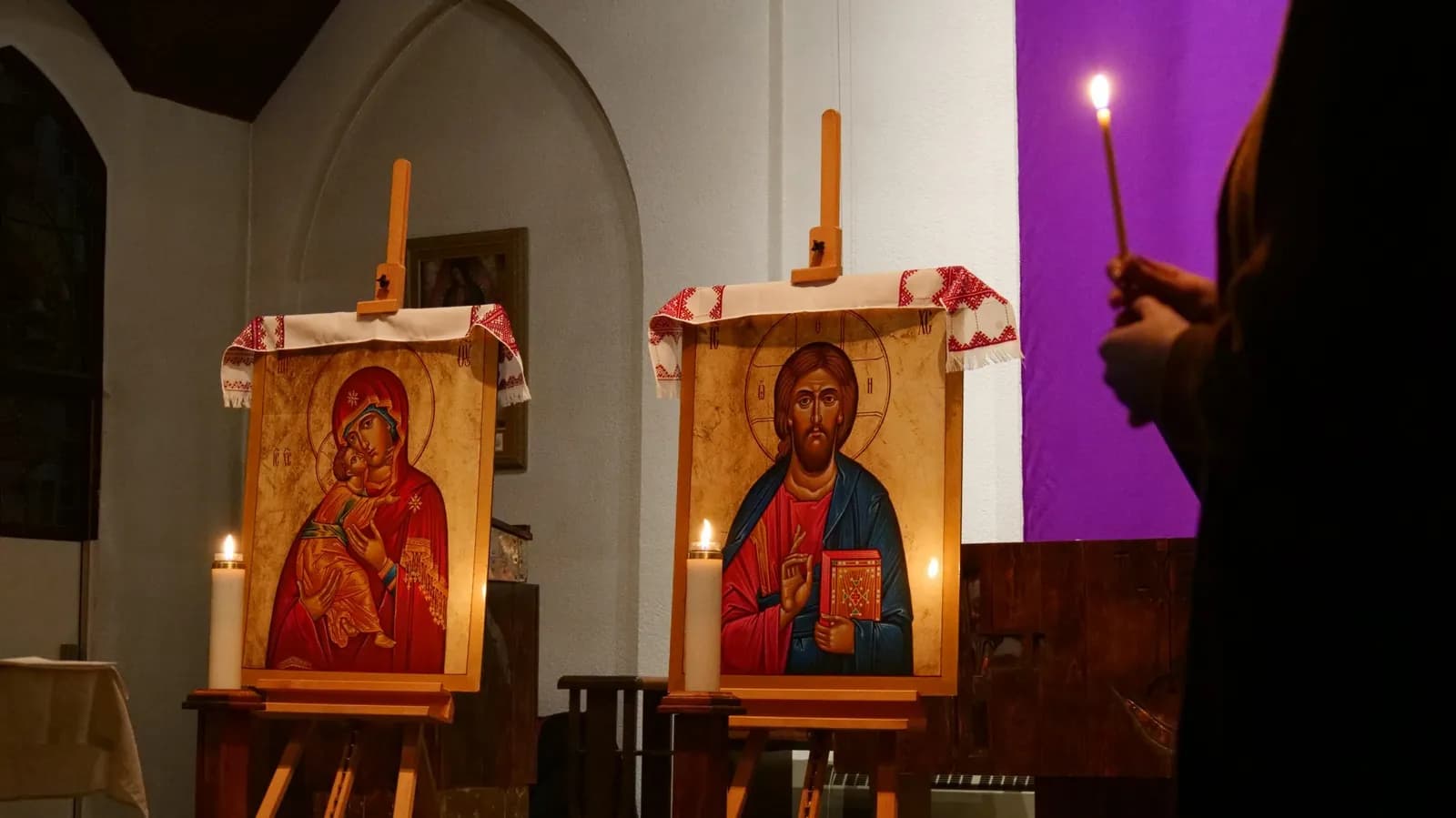 Two icons, Christ and the Theotokos, stand lit by candles in a church.
