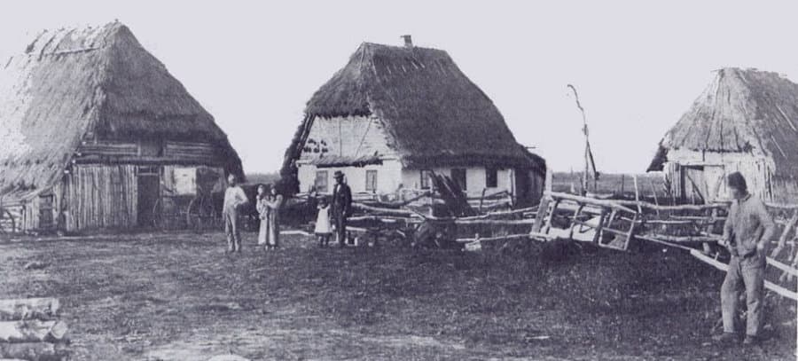 Rural homestead with thatched roofs and a family standing outside.