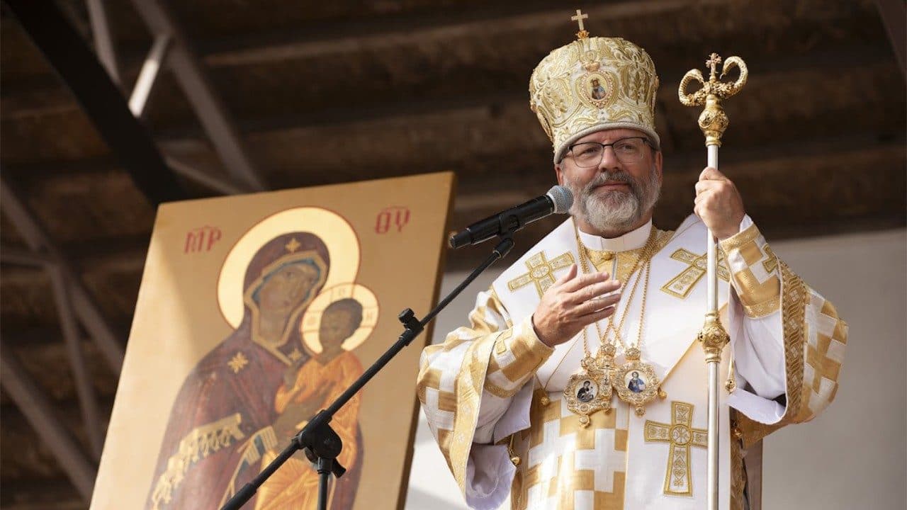 Bishop in ornate vestments and mitre holds a pastoral staff, with an icon of the Theotokos beside him.