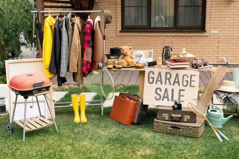 Garage sale with clothes, toys, books, and household items displayed on racks and tables.
