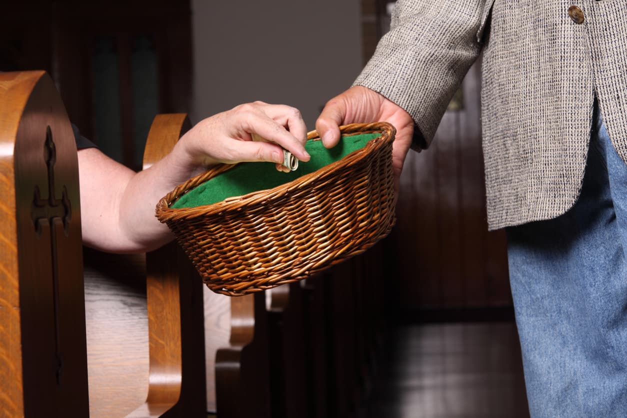 Hands place money into a collection basket held between church pews.