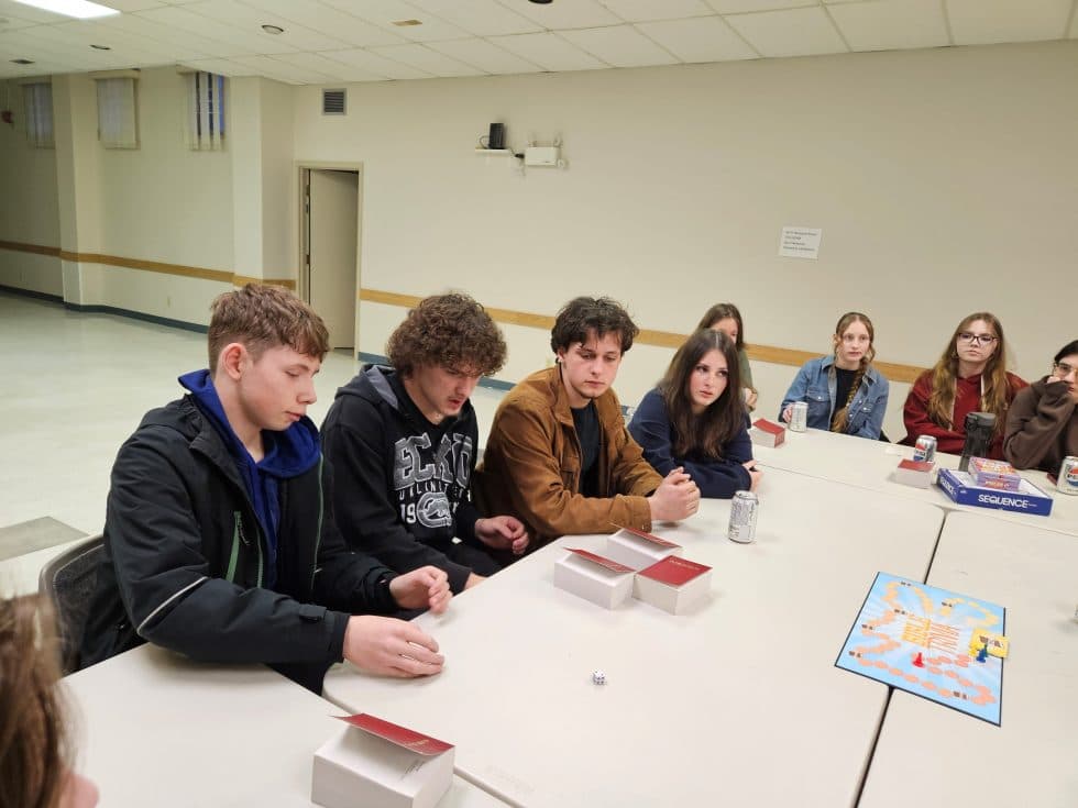 Youth gather around a table playing a board game 