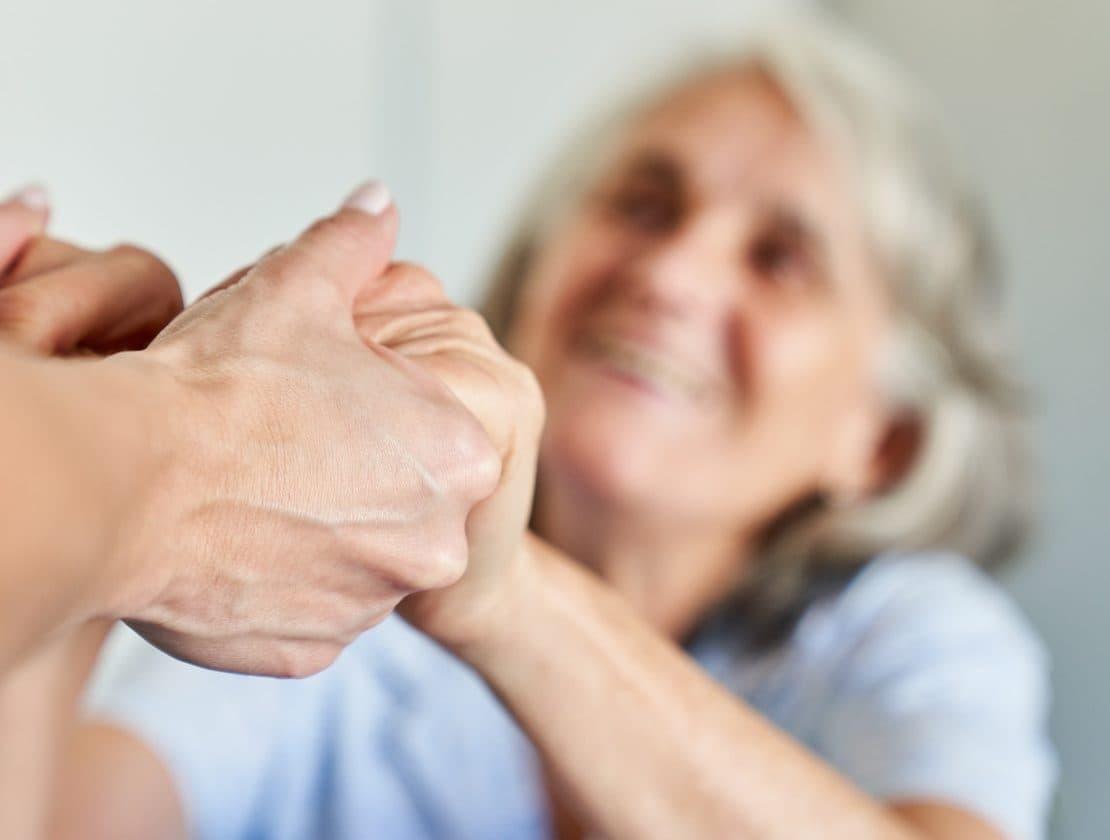 A caregiver holds an older woman’s hand.