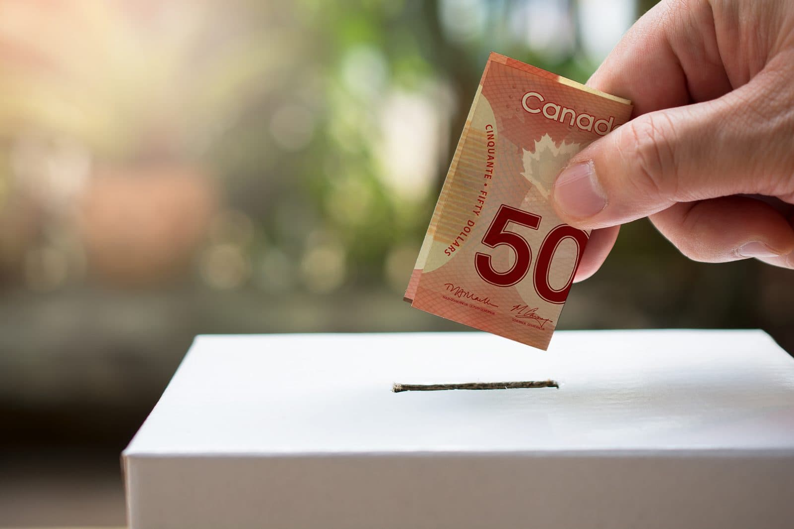 A hand places a Canadian fifty-dollar bill into a donation box.