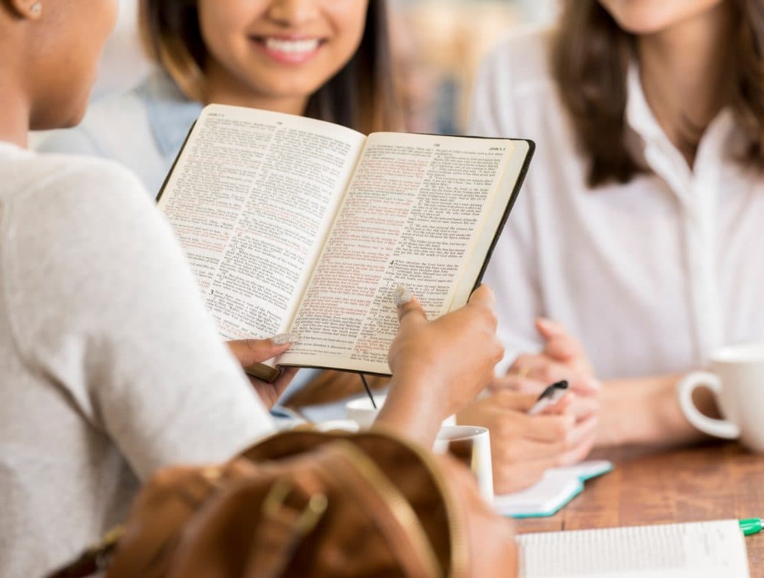 Adults gather around an open Bible during a small-group faith discussion.