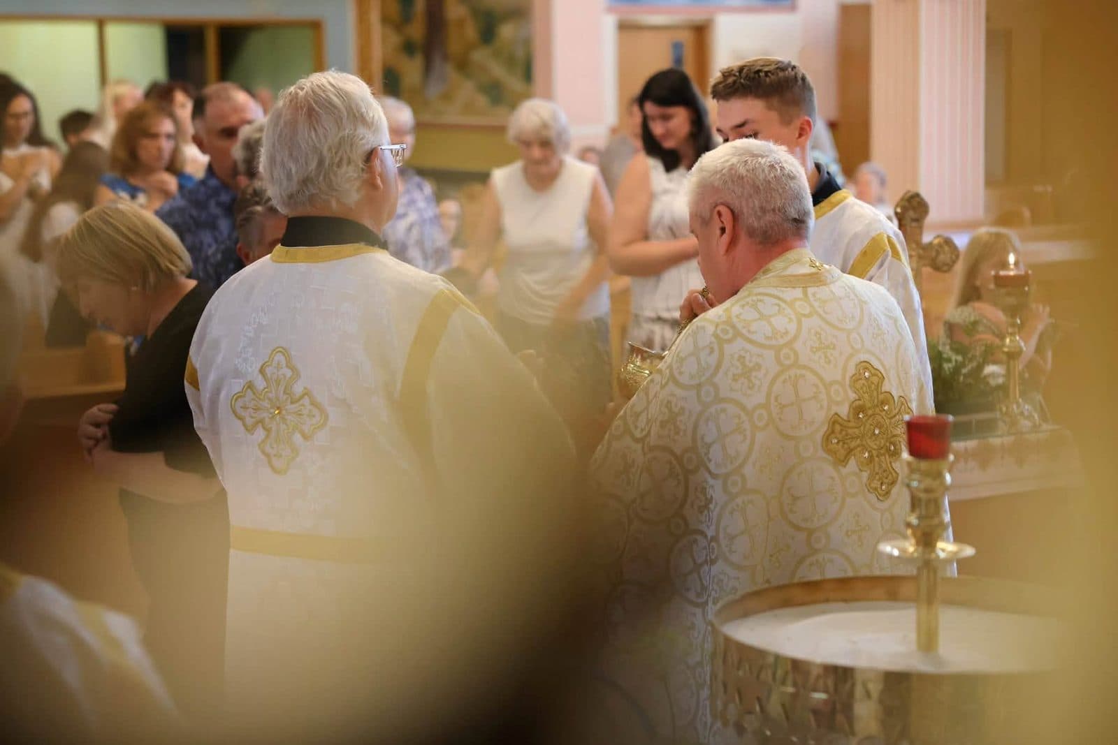 A priest serves worshippers during a sacramental service inside a warm, welcoming church.